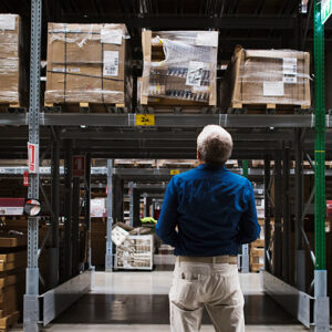 Man Stands In Front Of Large Inventory Shelves