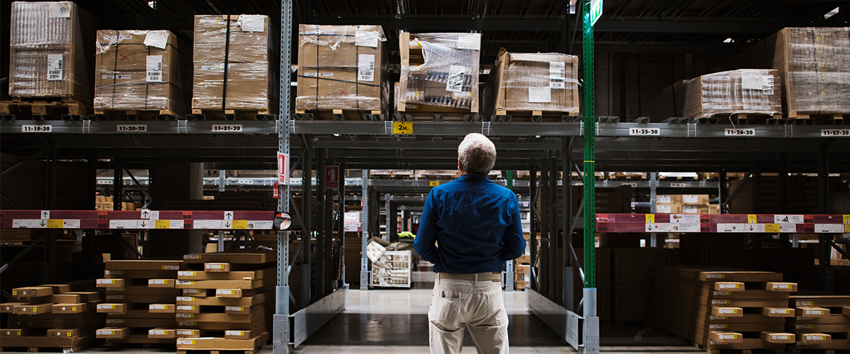 Man Stands In Front Of Large Inventory Shelves